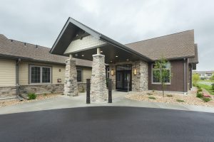 photo of entrance with roof overhang with brown siding, and brick columns