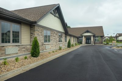 Side view of building with covered entrance and with asphalt drive way and brick and cream colored siding