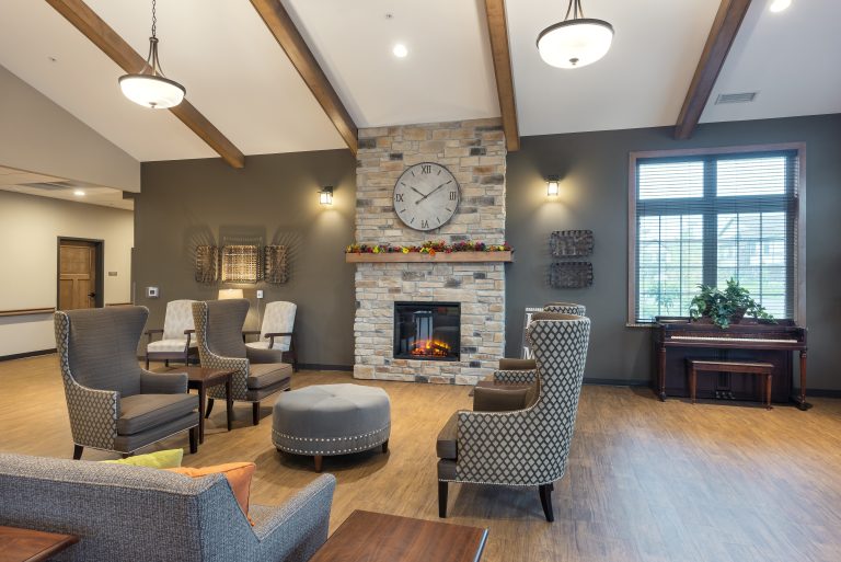 Lobby of retirement living facility with vaulted ceilings and a brick fireplace surrounded by lounge chairs and a couch