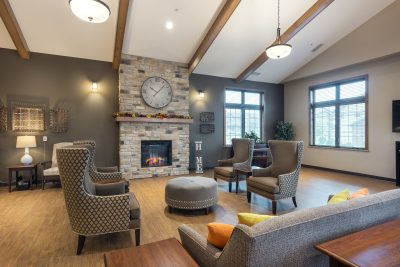 Lobby of retirement living facility with vaulted ceilings and a brick fireplace surrounded by lounge chairs and a couch