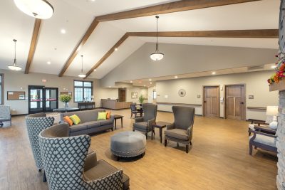 Lobby of retirement living facility with vaulted ceilings with wood beams and lounge chairs and a couch