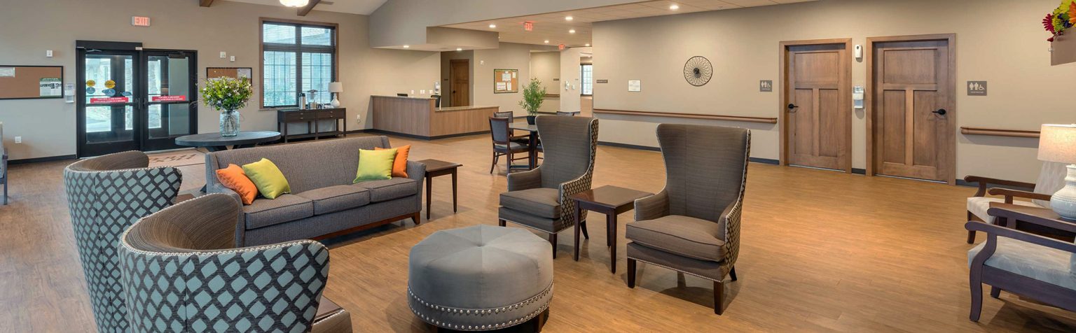 Lobby of retirement living facility with vaulted ceilings with wood beams and lounge chairs and a couch