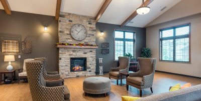 Lobby of retirement living facility with vaulted ceilings and a brick fireplace surrounded by lounge chairs and a couch