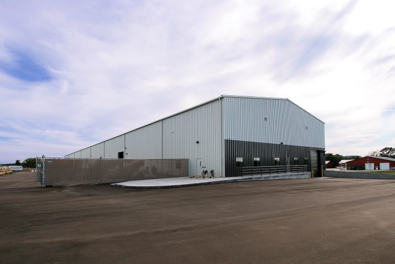 A large, modern warehouse building with a metal exterior. It has multiple loading docks and a spacious paved area