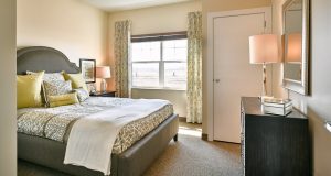 Independent senior living bedroom with large bed, window with light green curtains and cream colored walls