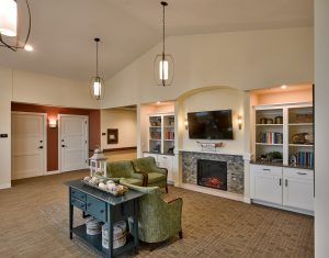 senior living area space with couches and a fireplace framed by white shelves and a tv above the fireplace