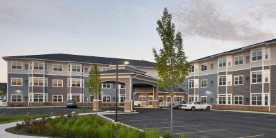 Exterior of three story senior living facility with covered entrance and blue and grey siding