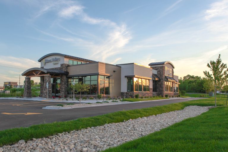 A modern bank with large windows and stone accents under a blue sky with wispy clouds. The foreground features a landscaped area with grass and a gravel path.