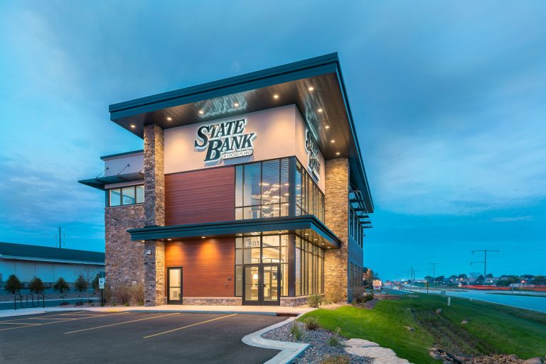 A modern two-story bank building at dusk showcases impressive architecture with large windows and a combination of brick and wood exterior.