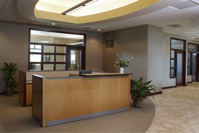 Bank lobby with a tiled floor, comfortable seating, a reception desk in the background, and a lit fireplace on the right. Potted plants add a touch of greenery to the space.