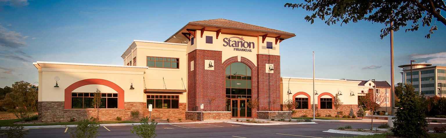 wide view of bank with brick exterior and tan colored plaster, large glass windows and an arch frame the entrance.