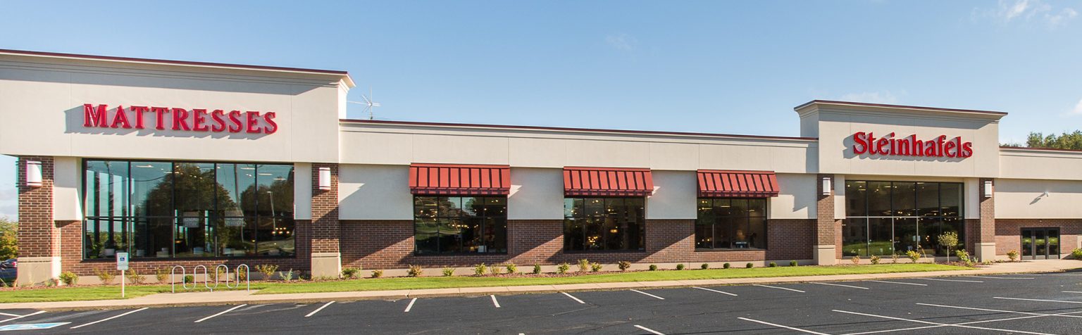 Exterior of retail furniture store with brick and cream colored siding, with red metal window awnings