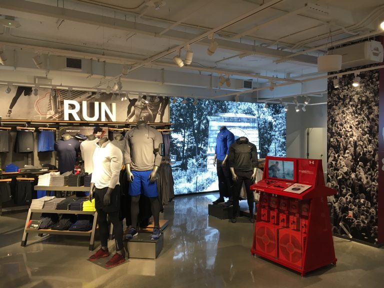 A sports clothing store display features mannequins in athletic gear, set against an outdoor running scene reminiscent of architectural landscapes.