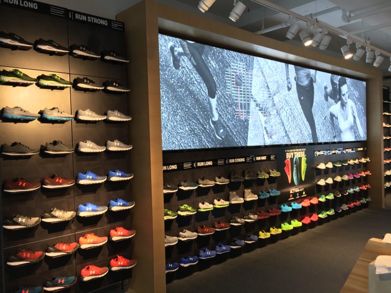 A retail store wall showcases a variety of running shoes in different colors