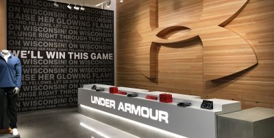 A modern retail store interior with a large logo on a wood-paneled wall. The opposite wall inspires shoppers with motivational phrases in black and white.