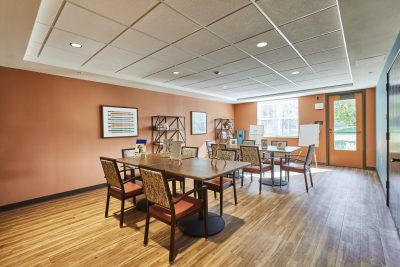 senior living facility crafting and art room with wood top tables, light orange walls, and art canvases on each table