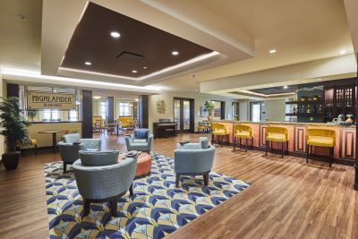 Senior living dining area with lounge seating, a bar area with yellow stools and a yellow and blue patterned rug