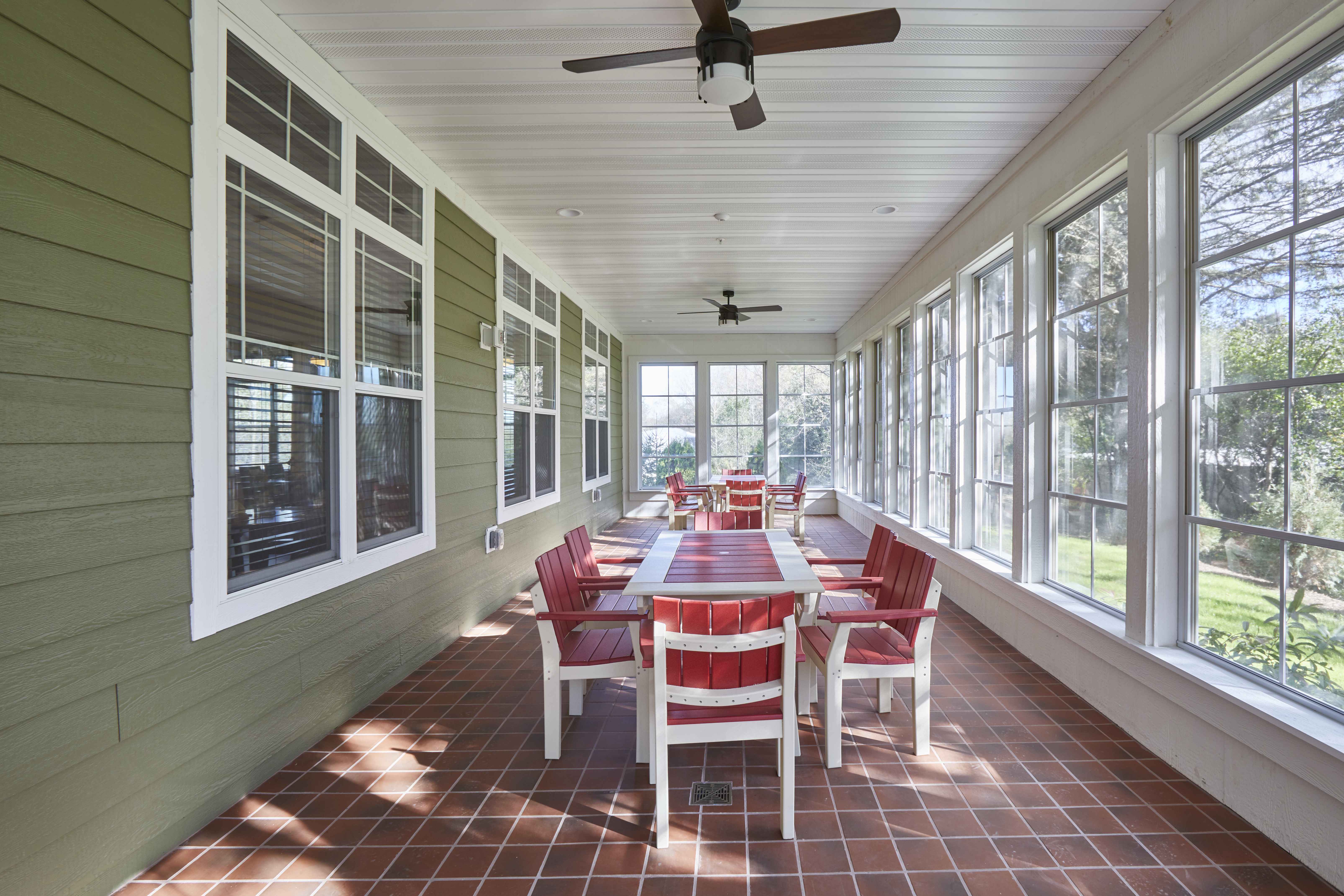 senior living facility enclosed patio with green siding, wrap around windows, white tables with burnt orange chairs