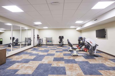 senior living facility fitness room with blue and tan patterned flooring, large mirrors and exercise equipment