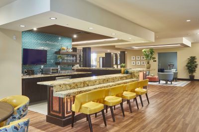 senior living facility bar with yellow stools, granite countertops, and teal colored backsplash