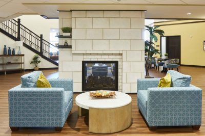 Senior living facility lounge area with cream stone fireplace with two light blue chairs on each side