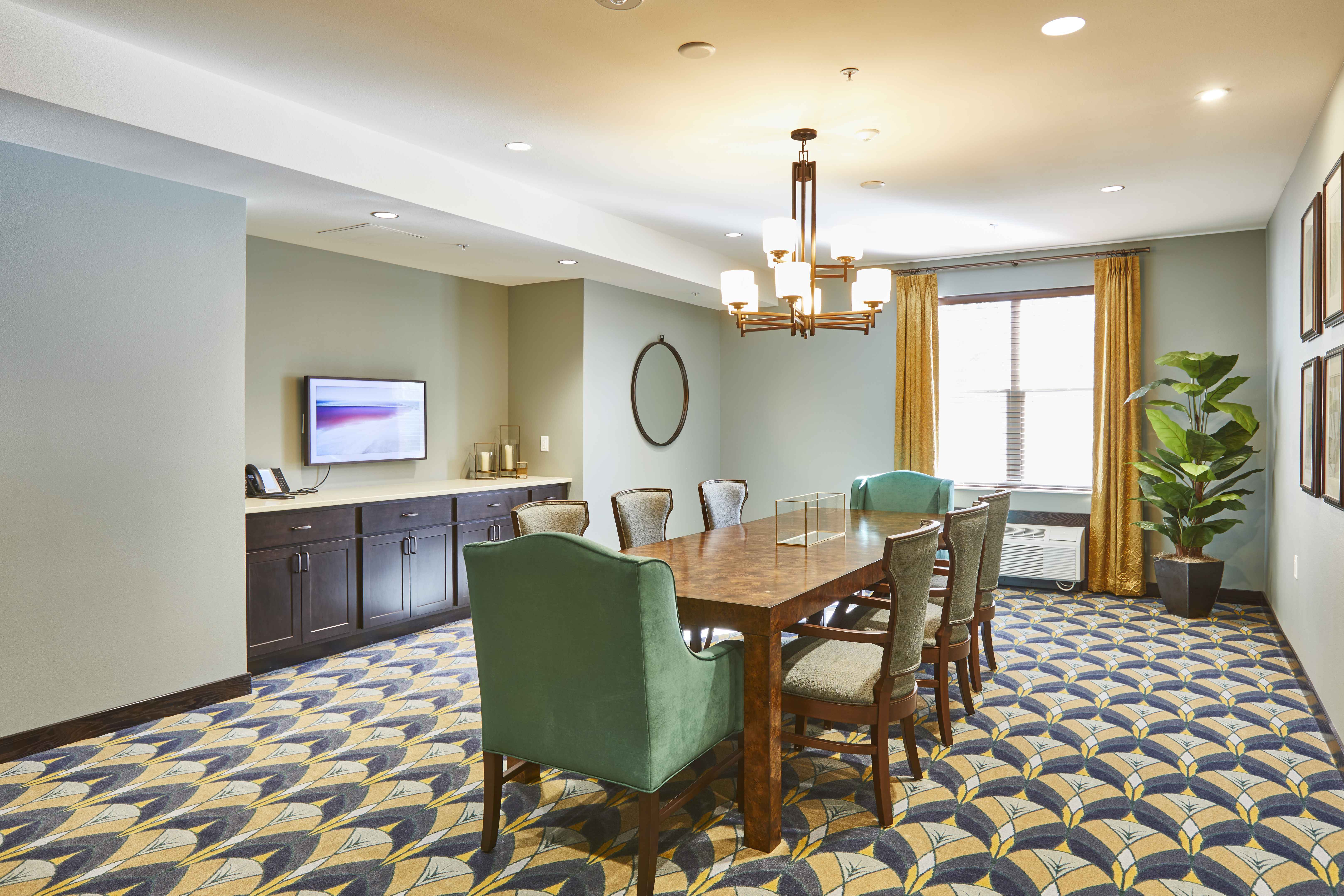 Senior living facility conference room with yellow and blue patterned carpet and a large wood conference table with green and tan chairs