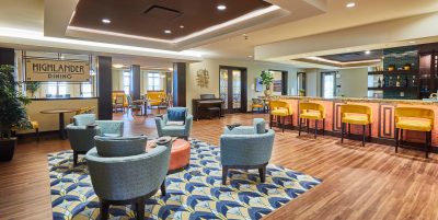 Senior living dining area with lounge seating, a bar area with yellow stools and a yellow and blue patterned rug