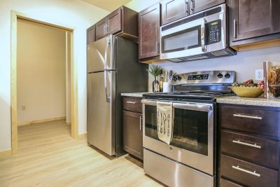 Kitchen in an apartment with stainless steel appliances, natural wood colored floors, and a microwave, oven and fridge