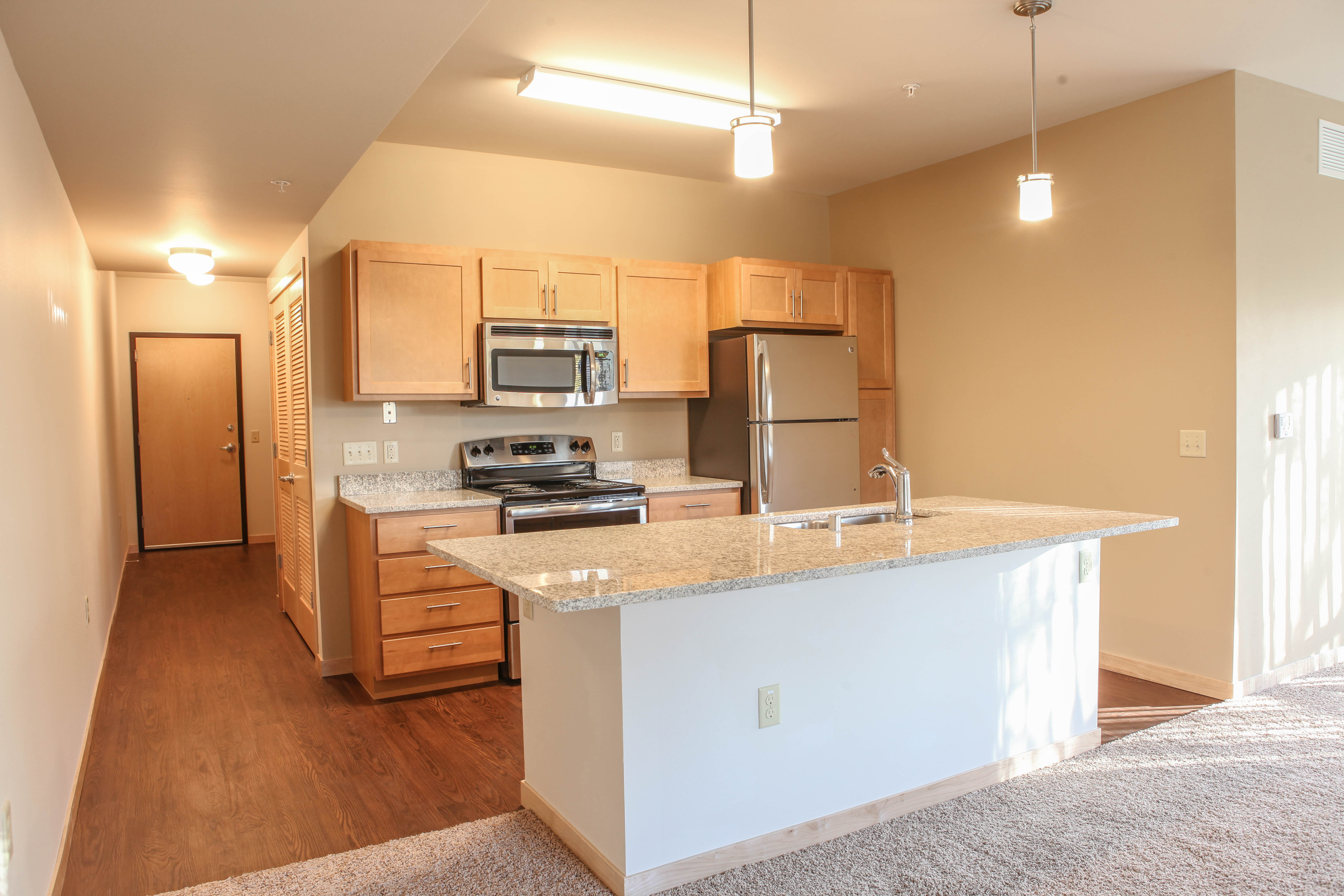 Apartment kitchen with shaker style light wood cabinets, pendant lighting over the island and light granite countertops