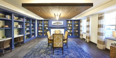 Senior Living facility library with wood floors, a blue carpet centering the room with blue book shelves a table and chairs