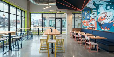 Sushi Restaurant with tables for seating, concrete flooring and mural wall with orange and blue accents