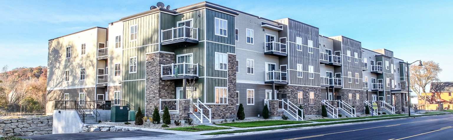 Exterior view from across the street of Multi-story apartment building with brick, cream and sage green siding