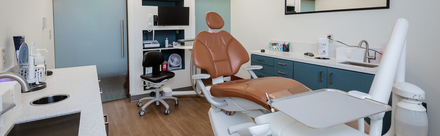 Dental lab with brown leather chair, glass doors and wood flooring