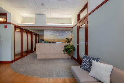 Fard Family Dental lobby renovated by Iconica, showcasing a modern reception desk, soft seating, wood flooring, and natural light that create a bright and welcoming dental office environment.
