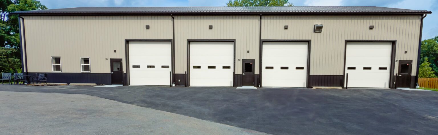 Metal panel industrial building front with four large overhead bay doors, personnel doors, and newly paved asphalt apron