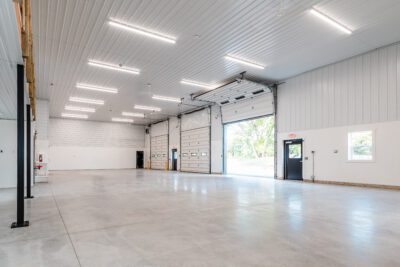 Bright warehouse interior with polished concrete floor, LED strip lighting, and multiple overhead doors—one open to the outside