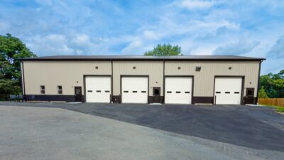 Metal panel industrial building front with four large overhead bay doors, personnel doors, and newly paved asphalt apron