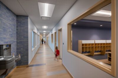Long school corridor with classroom windows and children walking.