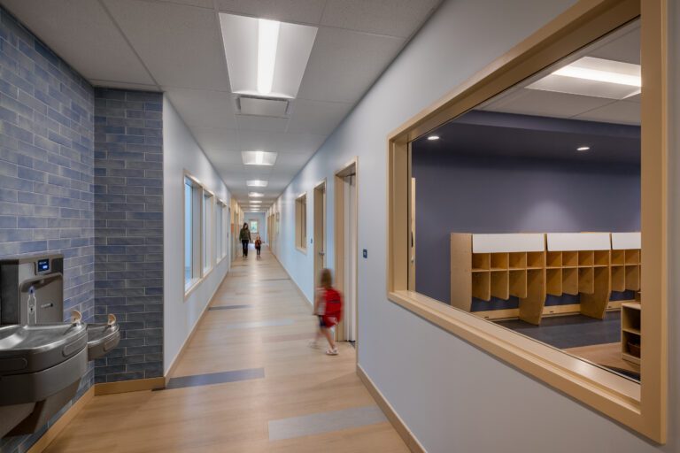 Long school corridor with classroom windows and children walking.