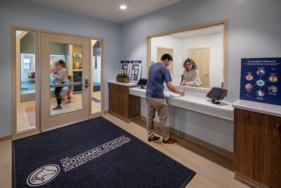 Secure school reception with staff at check-in counter and family entering.