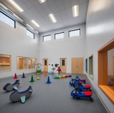 Indoor gym with play equipment, tall ceiling, and child running.