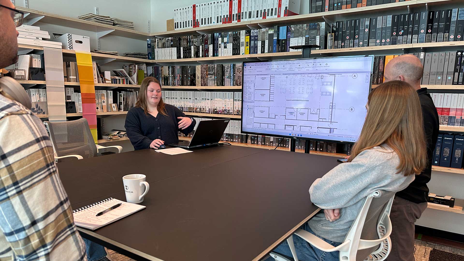 Iconica team member presenting floor plans on a large monitor during a conference room meeting with interns.