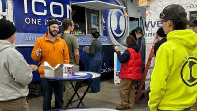 Iew From Inside The Iconica Food Truck Service Window Looking Out At Students Waiting To Order, With Trays Of GoMacro Protein Bars, Boxed Lunches, And Bottled Water Arranged On The Counter Ready To Be Served.