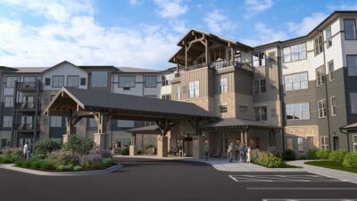 Rendering Of LilyRose Senior Living's Covered Main Entrance With Craftsman-style Timber Details, Stone Accents, And Residents Gathered Near The Welcoming Entryway.