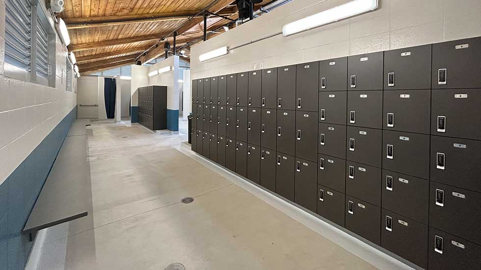 Interior of the remodeled locker room at Sheehan Park Family Aquatic Center, showing rows of new electronic keypad lockers, a wood ceiling, and a wide accessible walkway.