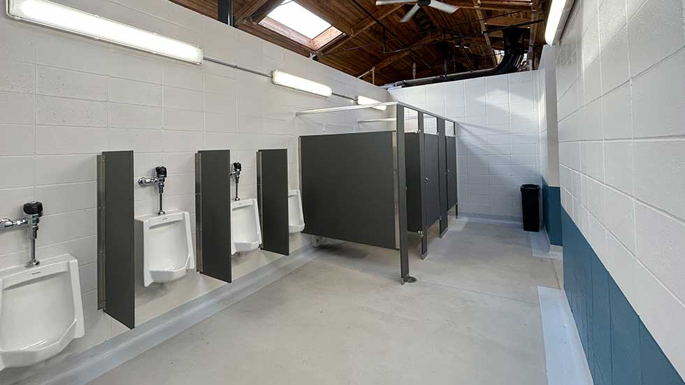 Remodeled men's restroom at Sheehan Park Family Aquatic Center with new urinals, tiled walls, and toilet stalls.