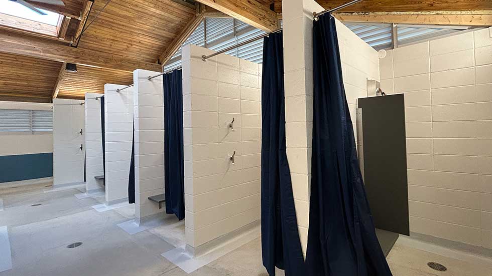 Remodeled shower stalls at Sheehan Park Family Aquatic Center with privacy curtains and a wood-beamed ceiling.