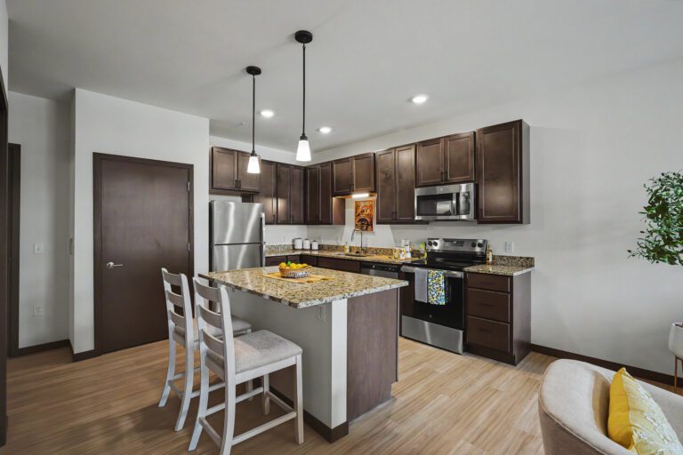 Vicino Apartments kitchen with granite island, stainless steel appliances, and dark wood cabinetry