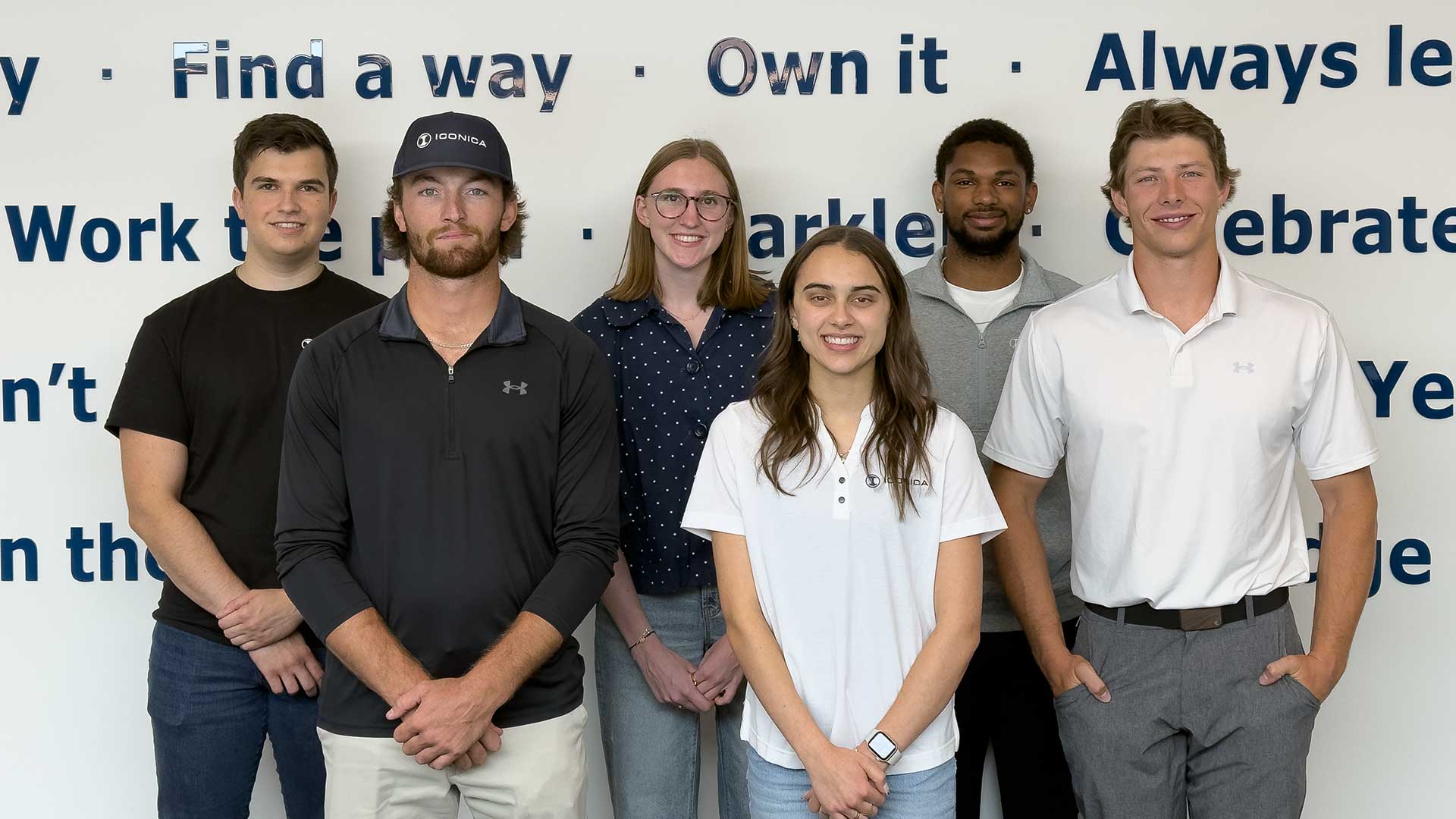 Group photo of six Iconica summer interns standing in front of a wall of company behaviors